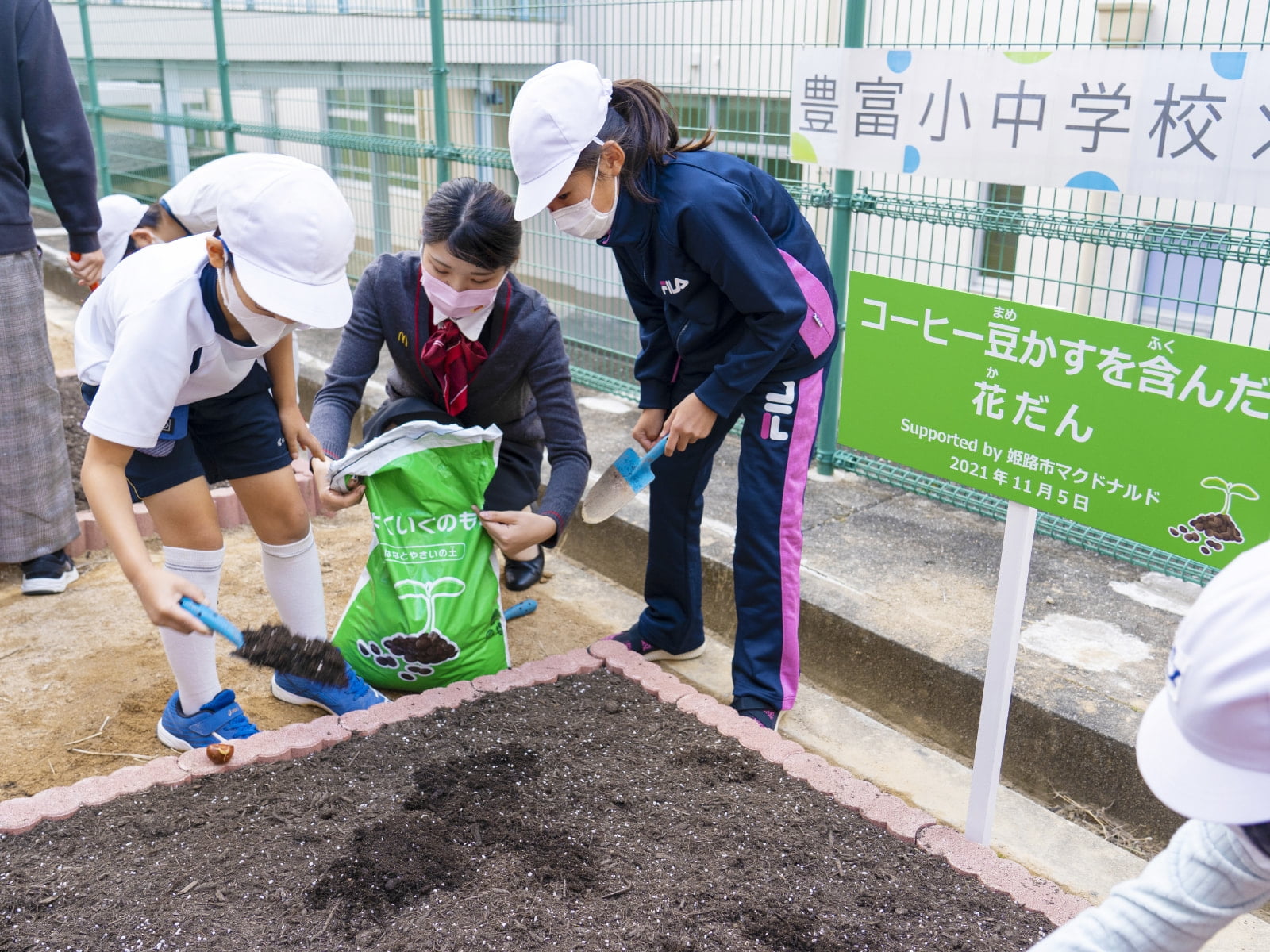 花壇にコーヒー豆かすのたい肥を撒く児童たち